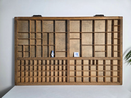 Oude drukkerijlade van hout met metalen handvatten, letterbak aan de muur.