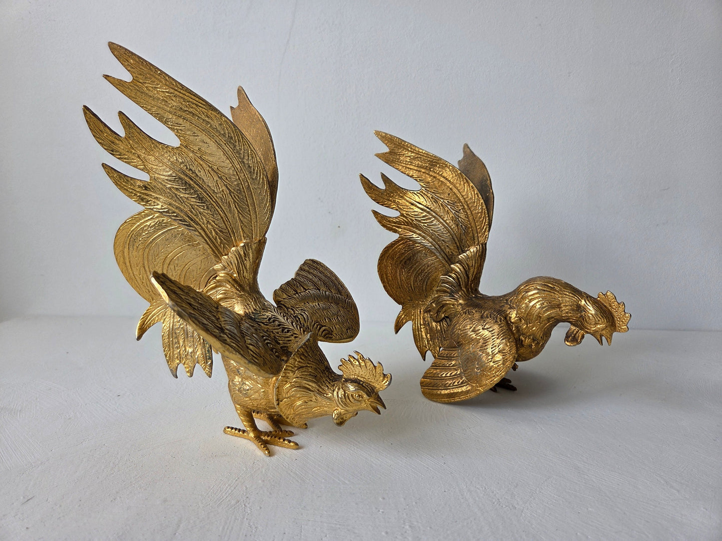 Set van twee goudkleurige metalen hanen in vechthouding op een witte ondergrond