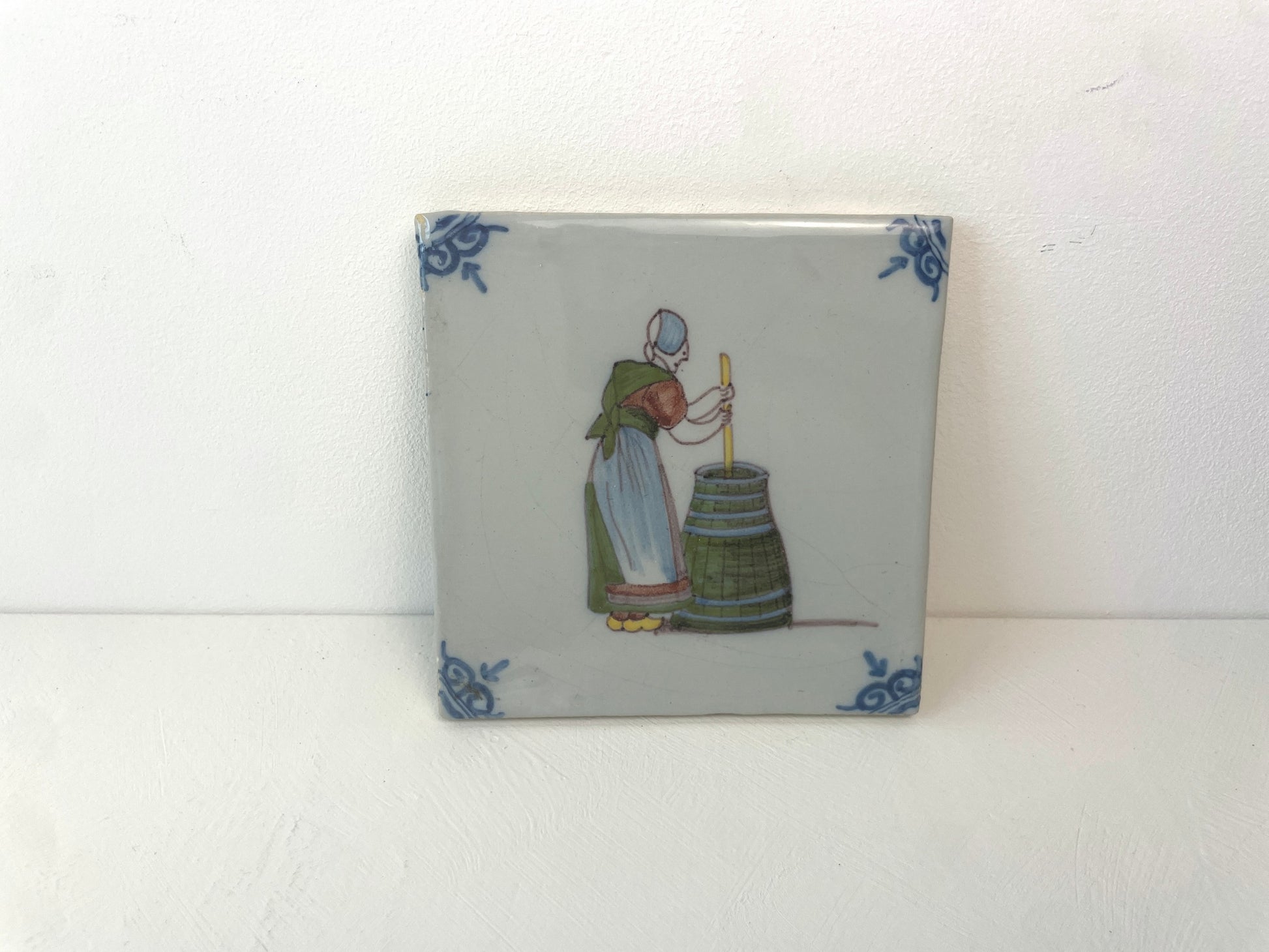 Handbeschilderde Nederlandse tegel van Makkum Tichelaar met vrouwelijk beroepstafereel.