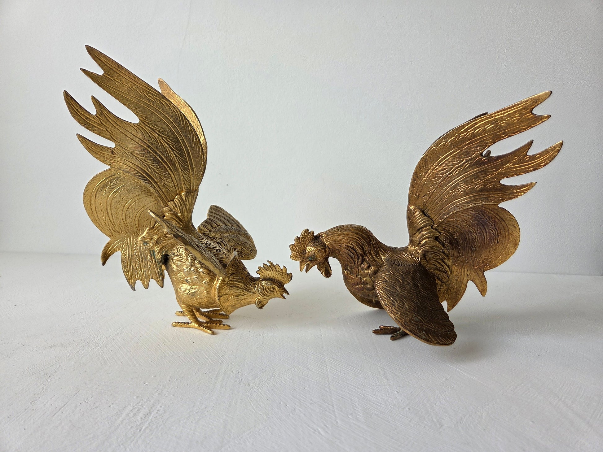 Goudkleurige metalen haanfiguren met sierlijke staarten en uitgespreide vleugels